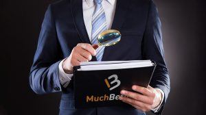 en mann holder en lupe over en bok med muchbetter-logoen på